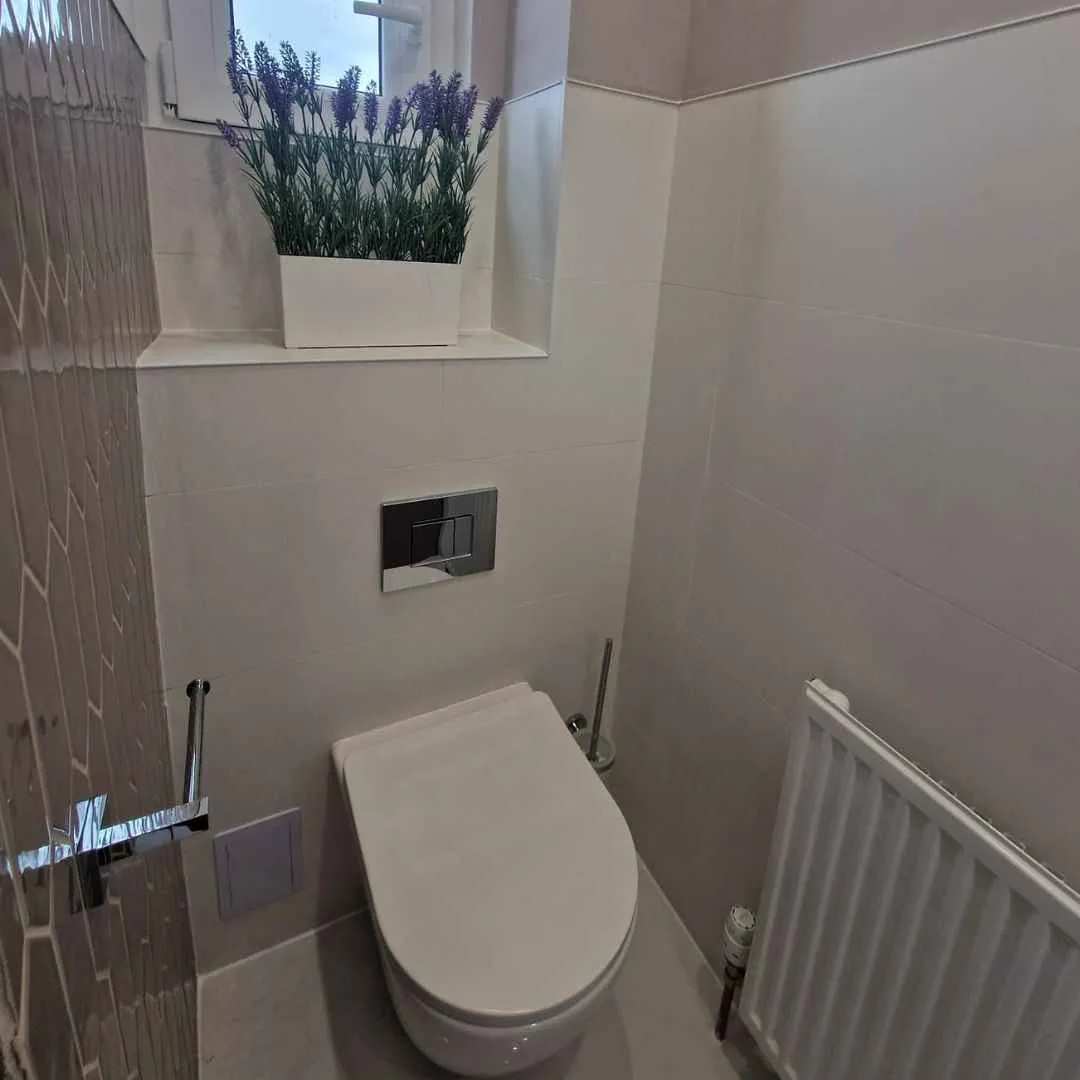 Wystrój małej łazienki z białymi płytkami, drewnianą zabudową i naturalną dekoracją roślinną - aranżacje łazienek komfort